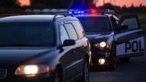 The police pull over a driver in the evening. A female officer approaches the stopped car and gets ready to test the driver, following Title 17 of the California Code of Regulations, rules for DUI chemical tests.
