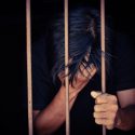 Man holding head behind prison bars