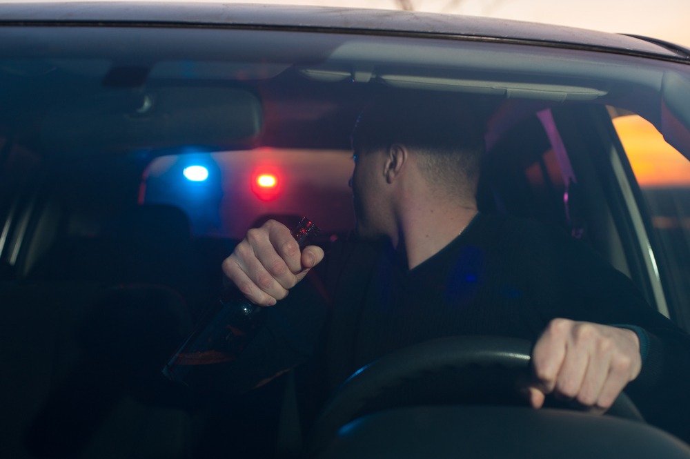 motorist holding bottle sees police lights behind him