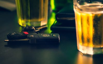 A pair of car keys next to a glass of liquor at a bar.