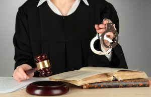 A judge sits with a gavel in one hand and handcuffs in the other.