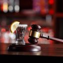 A shot of liquor next to a wooden gavel at a bar.