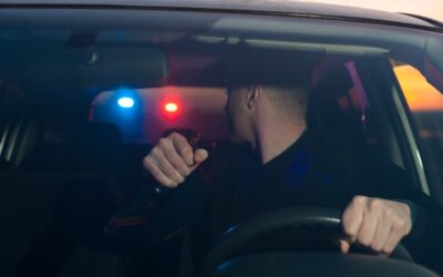 motorist holding bottle sees police lights behind him