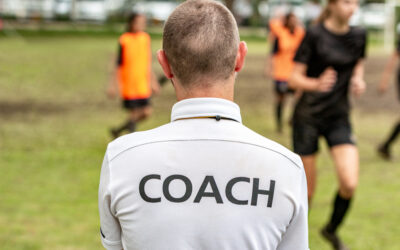 The back of a man wearing a white shirt with the word “Coach” written in black letters as he wonders if he can coach a youth sports team with a DUI.