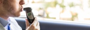 A man blows into a breathalyzer in his car and wonders if an ignition interlock device damages your car