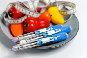 Several injection pens sit on a plate next to peppers and a measuring tape.