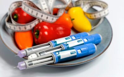 Several injection pens sit on a plate next to peppers and a measuring tape.