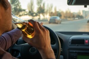 A man drinks an alcoholic beverage while behind the wheel of his vehicle while wondering about what happens after a first DUI in California.