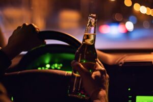 A driver holds a bottle of beer while driving to symbolize the question of what seven things you should know about a second offense DUI case.