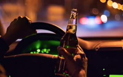 A driver holds a bottle of beer while driving to symbolize the question of what seven things you should know about a second offense DUI case.