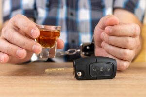 Hands hold a glass of alcohol and car keys. The person will later wonder about ways a lawyer can help with a DUI with injury case