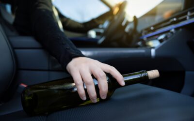 Close-up view of a driver holding a bottle of wine in the passenger seat to symbolize the question of whether a passenger can drink in a car.
